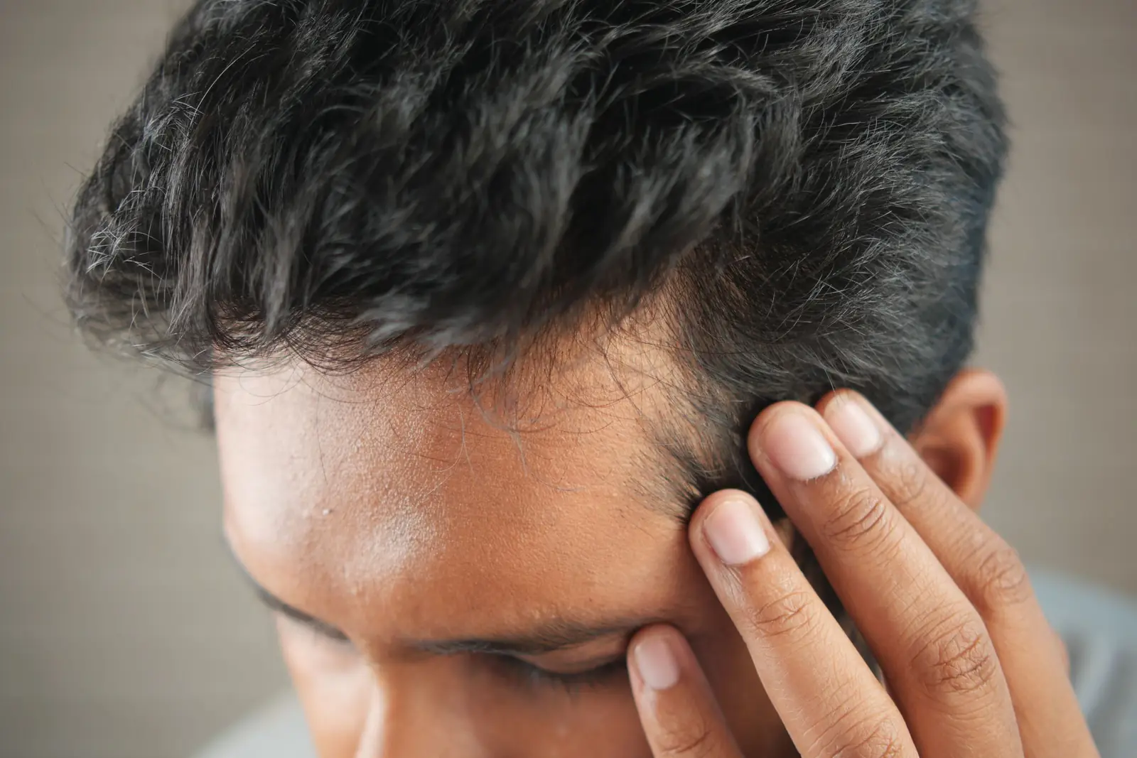 Close de homem com a mão na lateral da cabeça, tocando os fios escuros perto da linha do cabelo