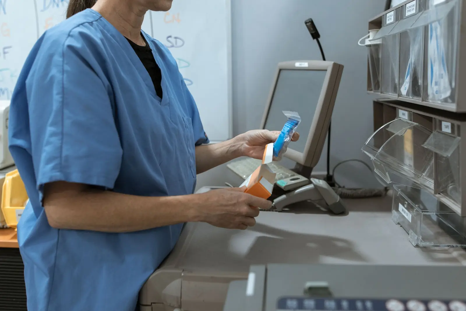 Profissional de farmácia, de rosto fora do quadro, confere a caixa de um medicamento no balcão de atendimento.