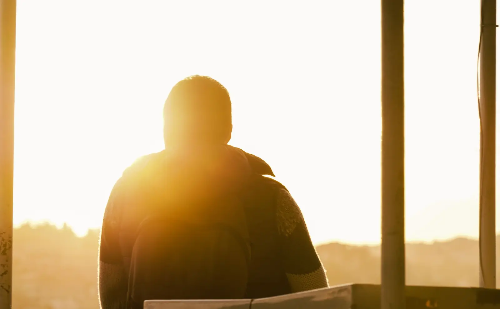 Silhueta de um homem visto de costas, em contraluz, diante do sol se pondo