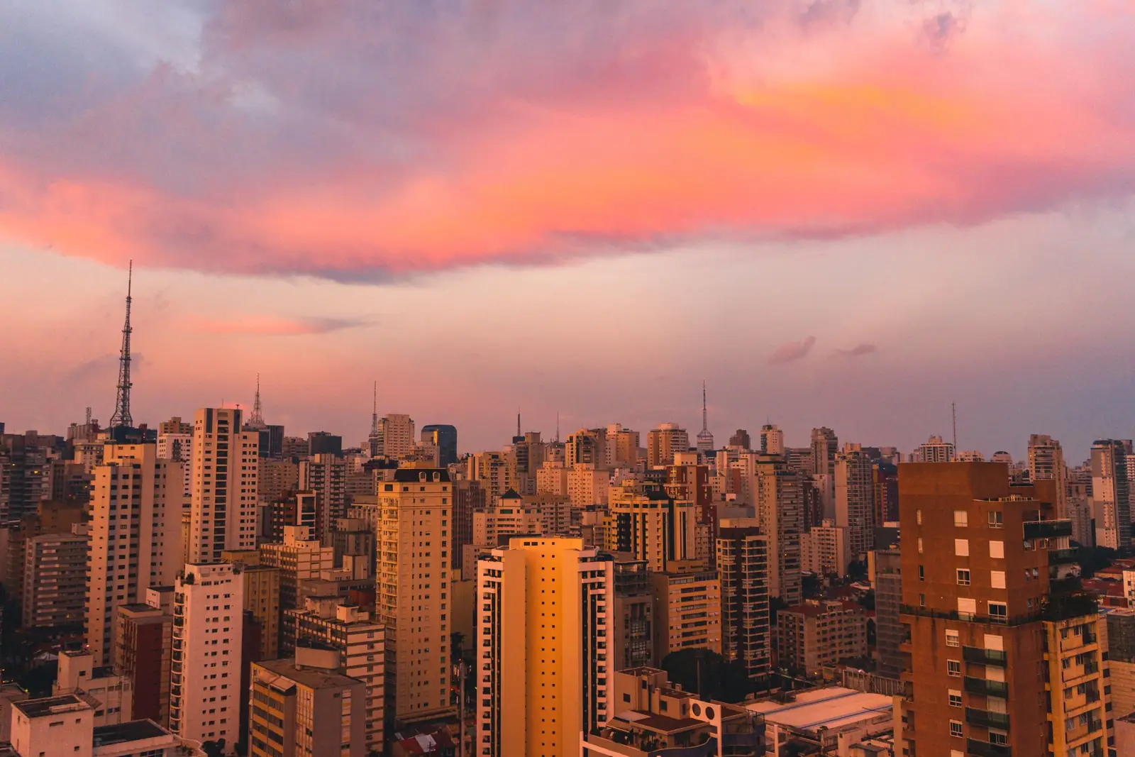 Prédios de uma grande cidade iluminados pela luz do entardecer, sob nuvens rosadas
