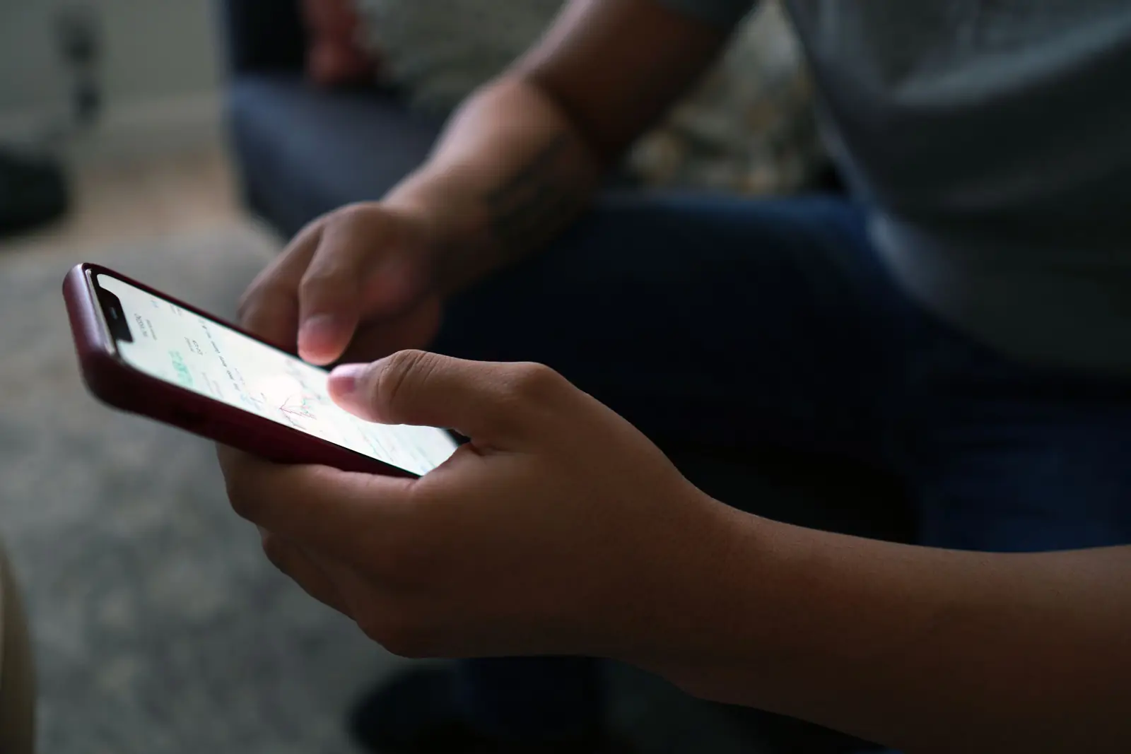 Mãos de um homem sentado digitando no celular, em ambiente doméstico com pouca luz